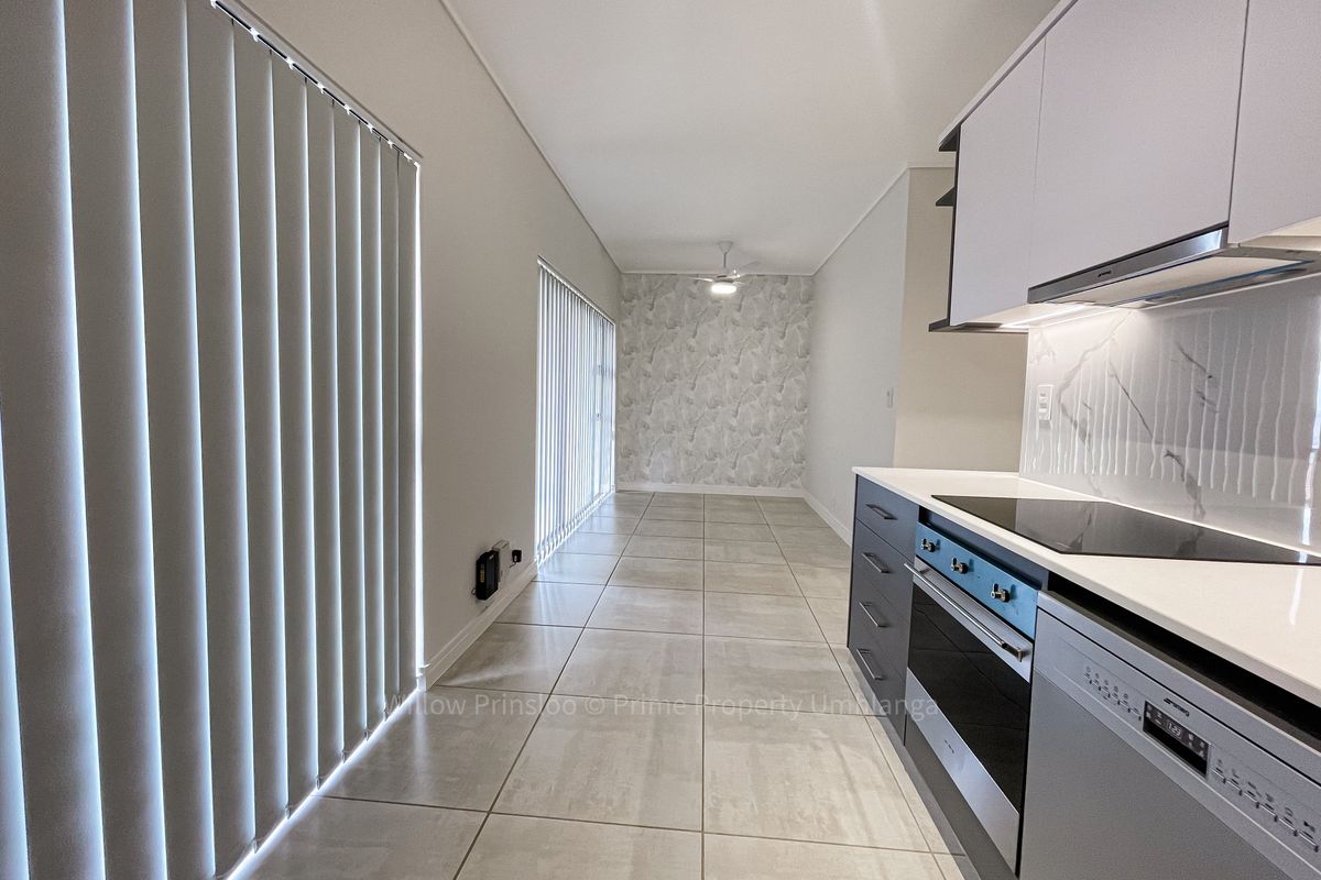 Modern open-plan kitchen and living area featuring sleek cabinetry, integrated appliances, marble-look splashback, tiled flooring, and large windows with vertical blinds.