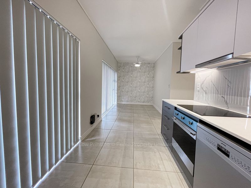 Modern open-plan kitchen and living area featuring sleek cabinetry, integrated appliances, marble-look splashback, tiled flooring, and large windows with vertical blinds.