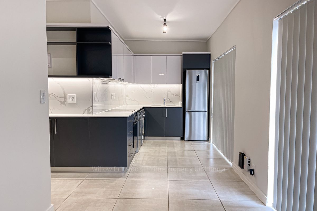 Modern kitchen featuring sleek two-tone cabinetry, marble-look splashbacks, integrated appliances, and neutral tiled flooring in a clean, contemporary apartment setting.