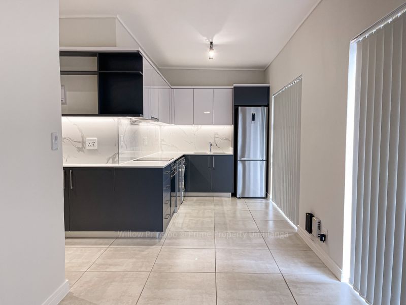 Modern kitchen featuring sleek two-tone cabinetry, marble-look splashbacks, integrated appliances, and neutral tiled flooring in a clean, contemporary apartment setting.
