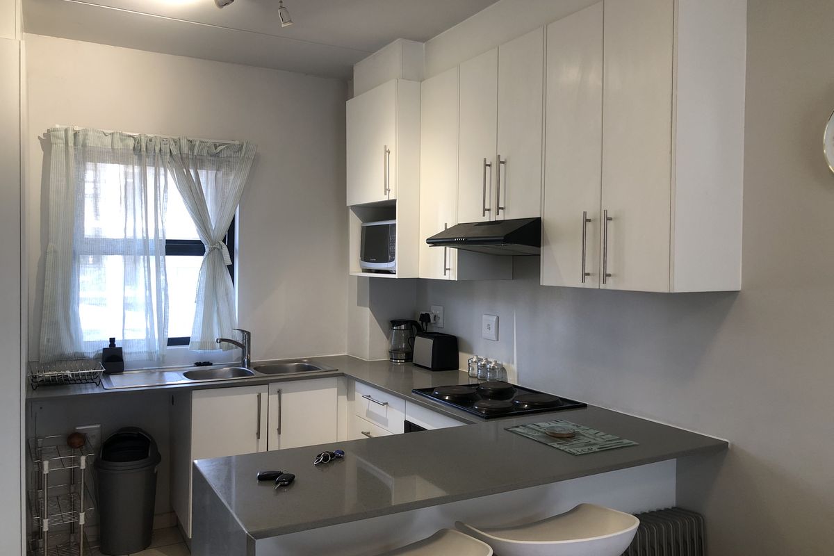 A functional kitchen featuring white cabinetry, stone countertops, a built-in hob with extractor fan, and a breakfast bar area.