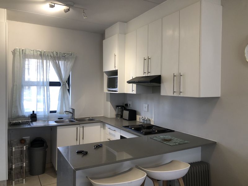 A functional kitchen featuring white cabinetry, stone countertops, a built-in hob with extractor fan, and a breakfast bar area.