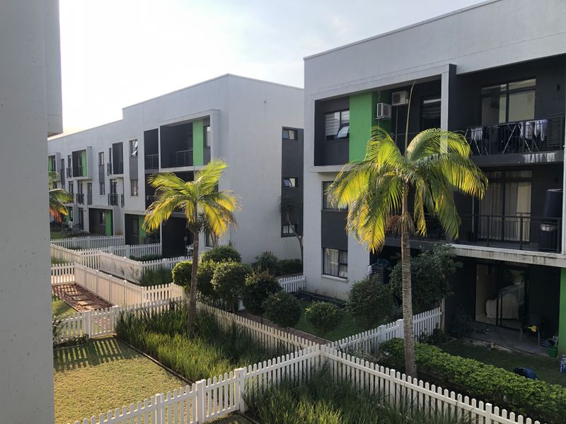 A view of the apartment complex rear elevation featuring modern architecture, private balconies, and well-maintained garden areas with white picket fencing.