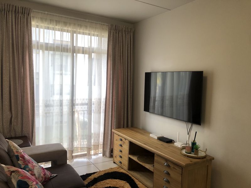 A well-maintained living room featuring tiled flooring and a large sliding glass door that provides access to the balcony.