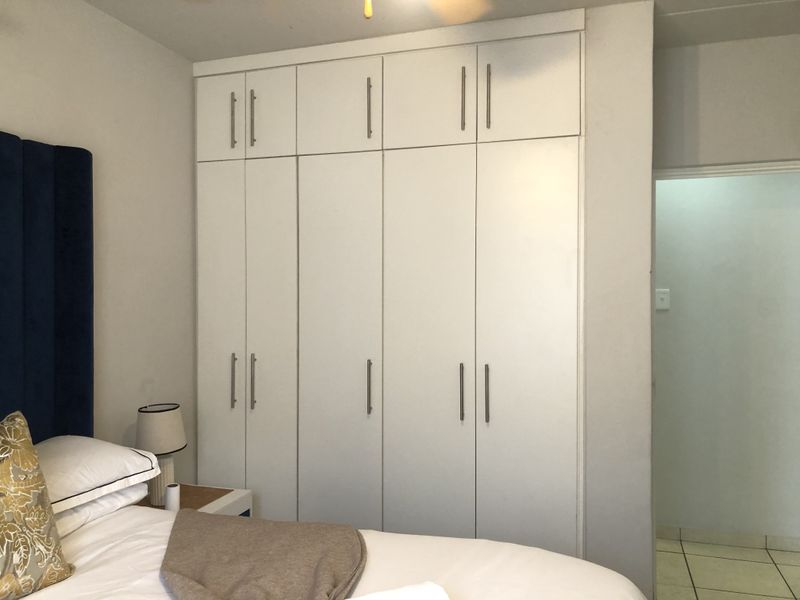 A bedroom featuring floor-to-ceiling white built-in cupboards providing ample storage space and a ceiling fan for climate control.