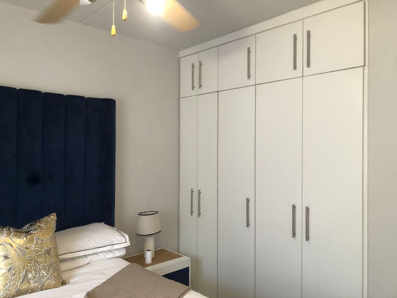 A well-maintained bedroom featuring floor-to-ceiling white built-in cupboards and a ceiling fan, providing ample storage and comfortable climate control.