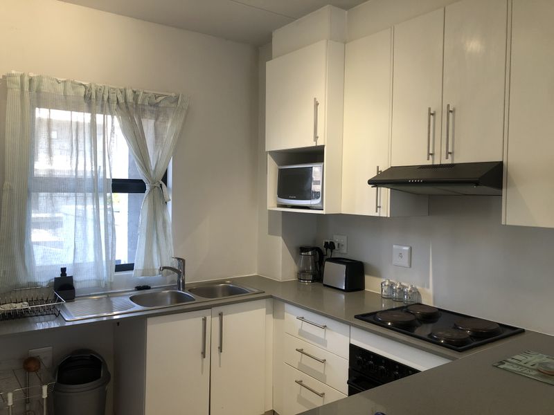 A functional kitchen featuring white cabinetry, grey stone countertops, a stainless steel double sink, and integrated appliances including an oven and hob.
