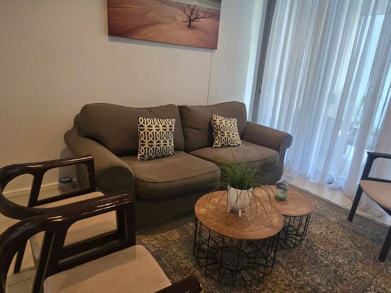 A comfortable living room area featuring tiled flooring and large sliding glass doors with sheer curtains, providing access to the outdoor space.