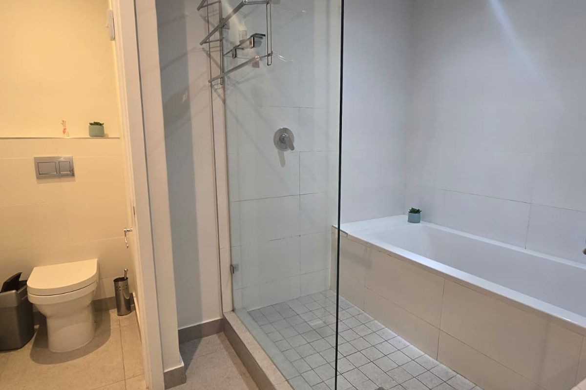 Modern bathroom featuring a wall-hung toilet with concealed cistern, a glass-enclosed shower, and a built-in bathtub with clean tiled finishes.