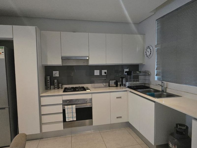 Modern kitchen featuring white cabinetry, stone countertops, gas hob, electric oven, and stainless steel sink with tiled flooring and venetian blinds.