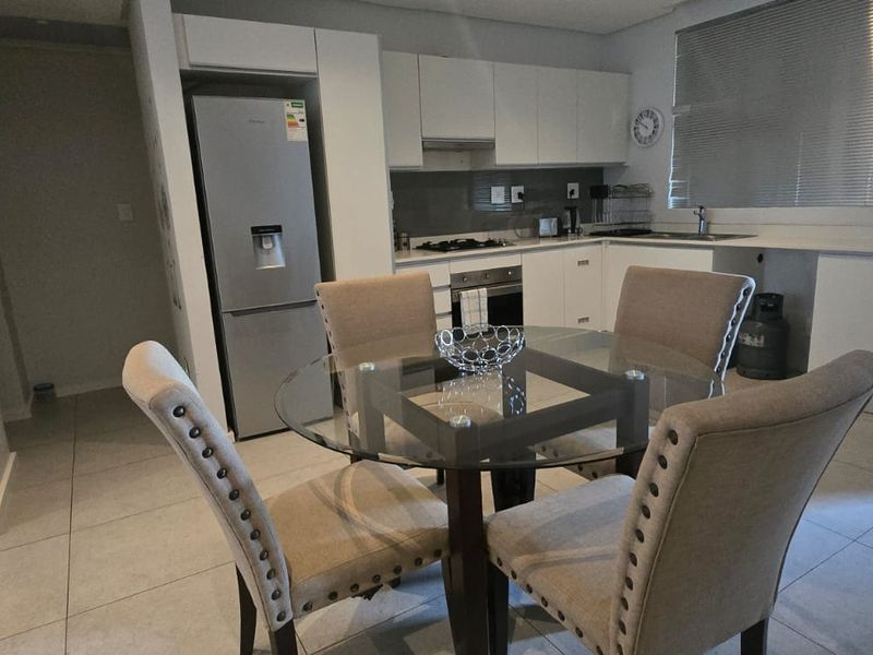 Modern open-plan kitchen featuring sleek white cabinetry, integrated appliances, and tiled flooring, seamlessly flowing into the dining area.