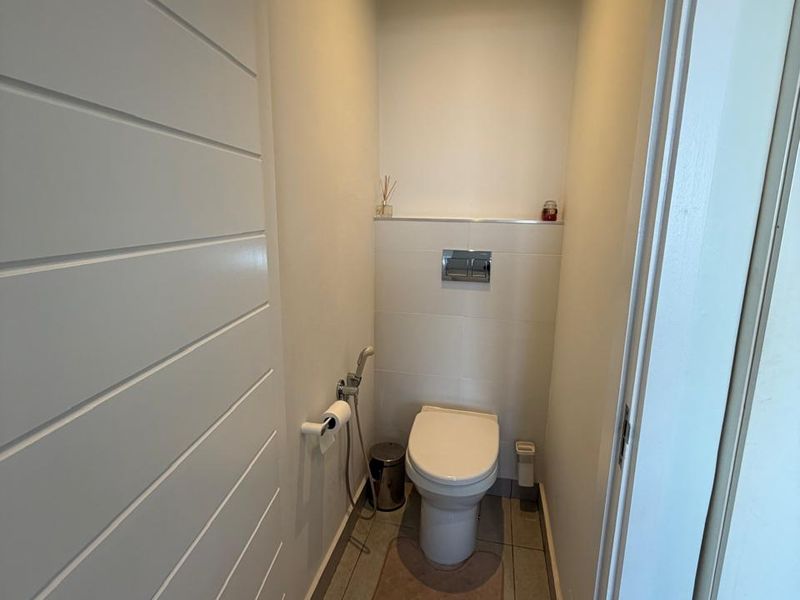 A compact, modern guest bathroom featuring a wall-mounted toilet with a concealed cistern and neutral floor tiling.
