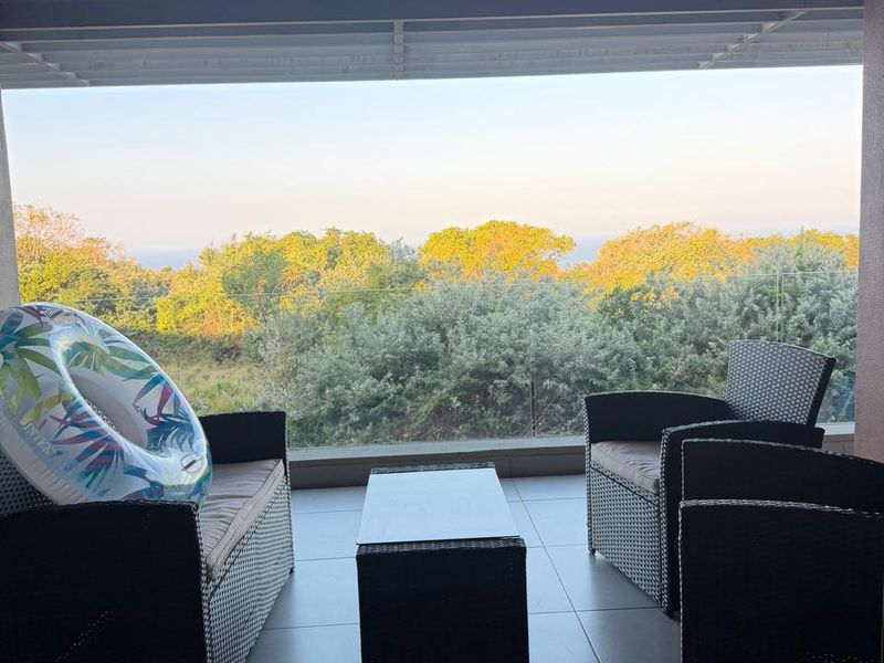 A covered balcony featuring tiled flooring and a glass balustrade, offering scenic views of the surrounding greenery.