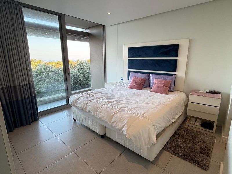 A modern bedroom featuring large floor-to-ceiling sliding glass doors, tiled flooring, recessed lighting, and integrated ducted air conditioning.