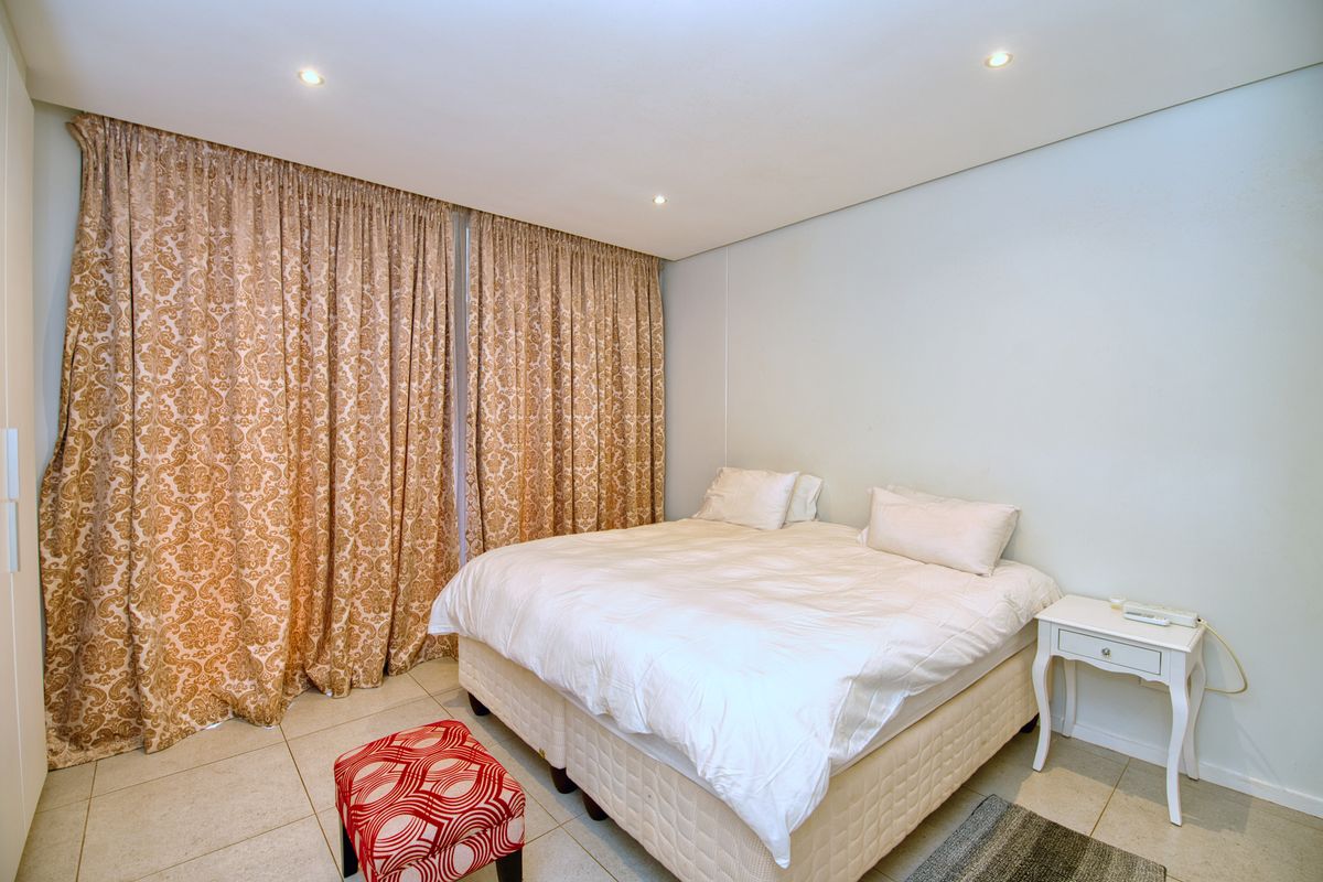 A well-lit bedroom featuring tiled flooring, recessed downlighting, and a built-in wardrobe, offering a clean and functional living space.