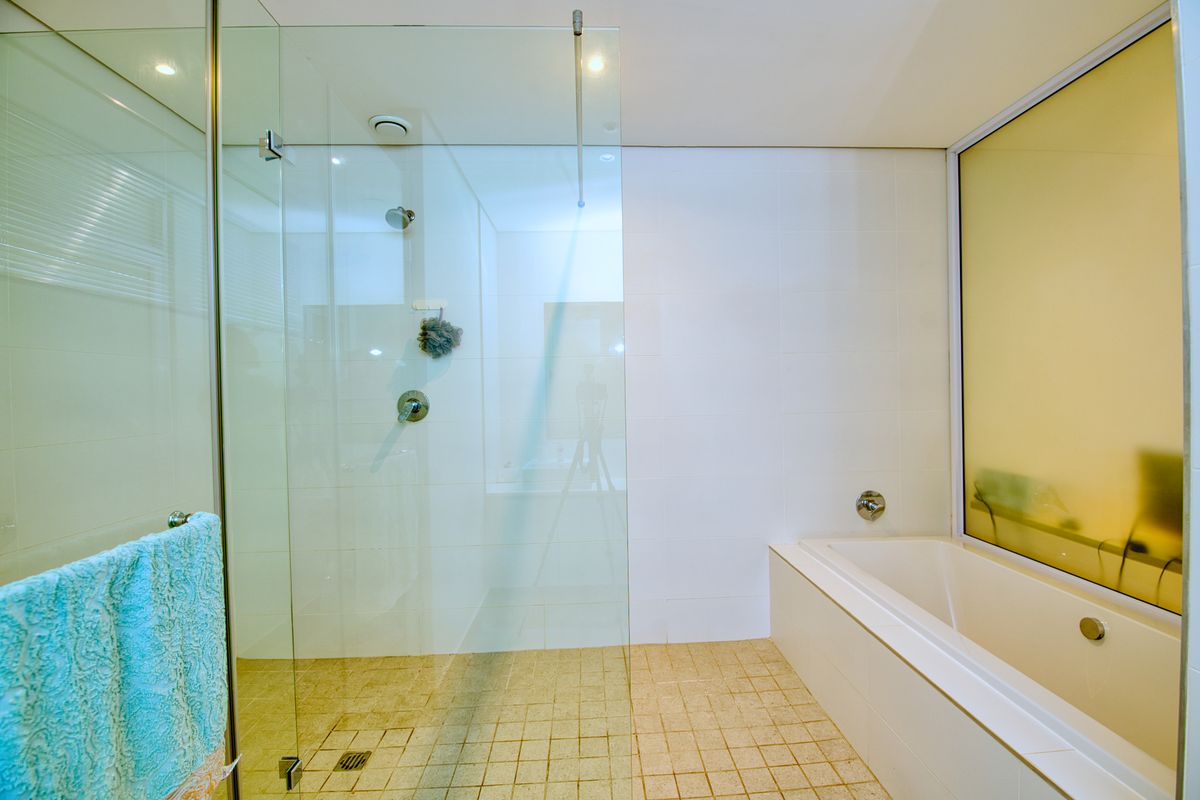 Modern bathroom featuring a glass-enclosed shower, a built-in bathtub, and neutral tiled finishes, offering a clean and functional space.