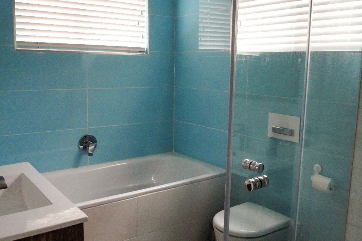 A functional bathroom featuring a built-in bathtub, wall-mounted toilet, glass shower enclosure, and a vanity unit with blue wall tiling.