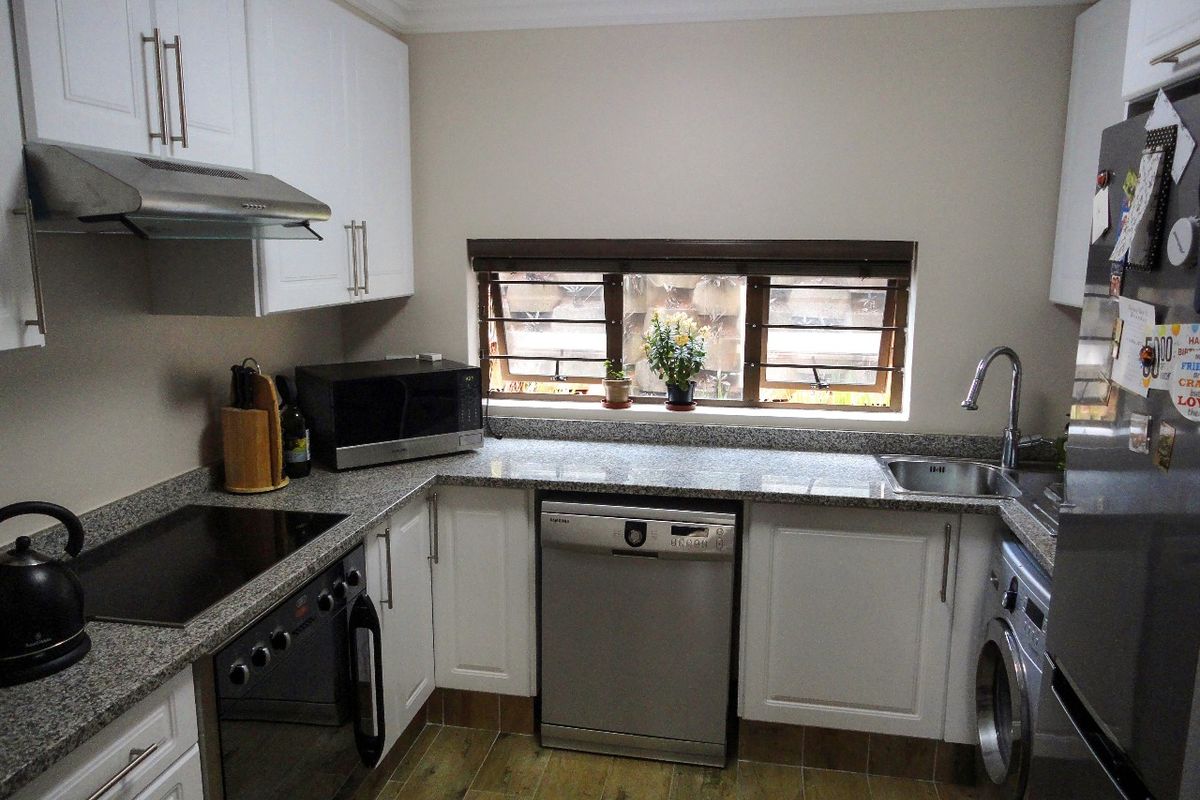 A well-maintained kitchen featuring white shaker-style cabinetry, granite countertops, integrated appliances, and tiled flooring with a functional layout.