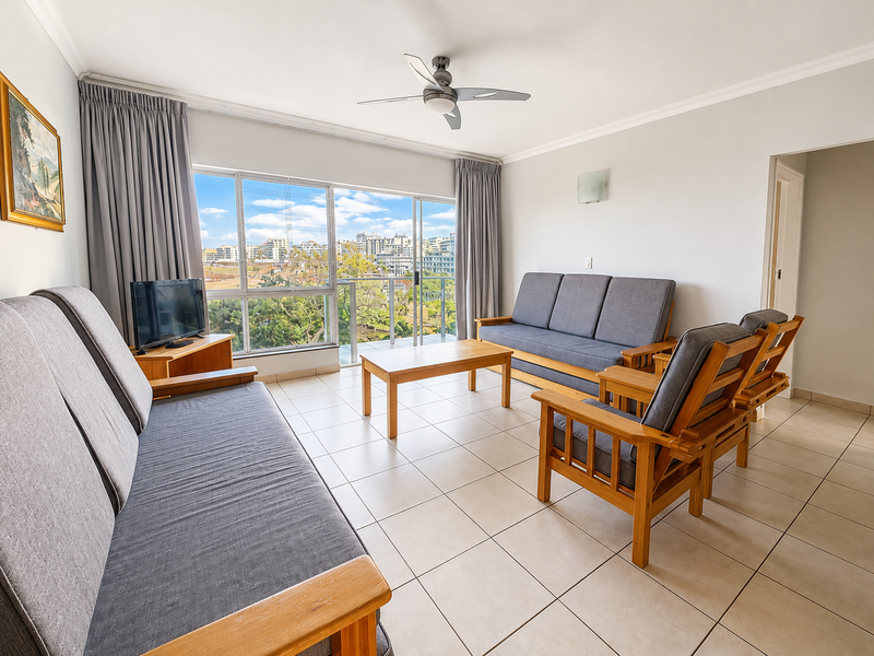 A bright living room featuring tiled flooring, a ceiling fan, and large sliding glass doors that open onto a balcony with urban views.
