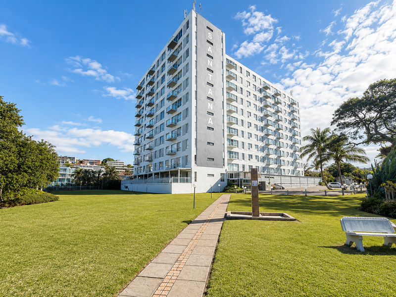 A clear exterior view of the Santana apartment building, featuring a well-maintained lawn, paved walkway, and multiple private balconies.