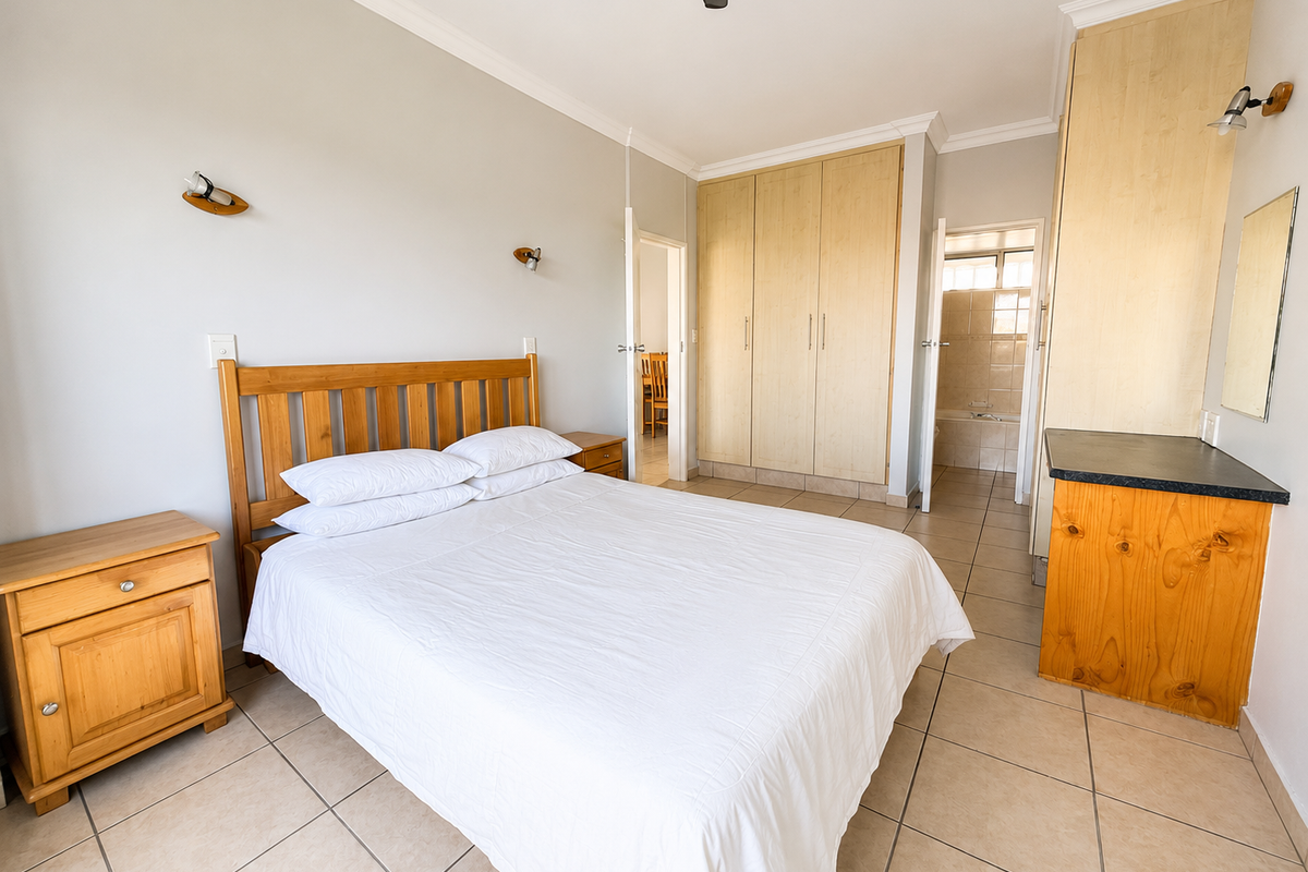 A well-lit bedroom featuring built-in wooden cupboards, tiled flooring, a ceiling fan, and direct access to an en-suite bathroom.