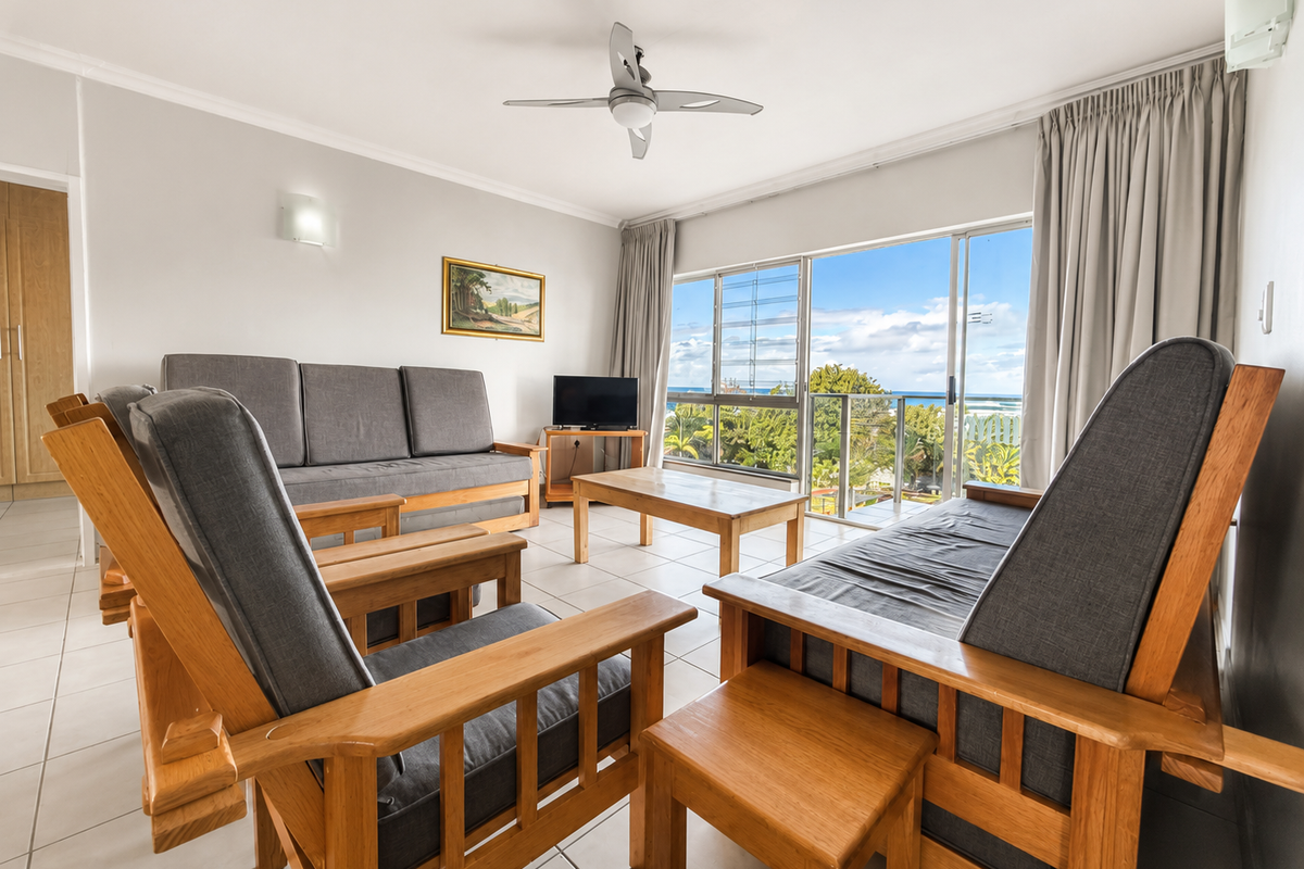 A bright living room featuring tiled floors, a ceiling fan, and large sliding doors opening to a balcony with scenic views.