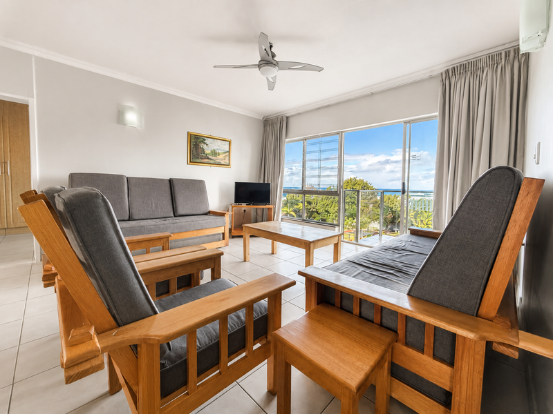 A bright living room featuring tiled floors, a ceiling fan, and large sliding doors opening to a balcony with scenic views.
