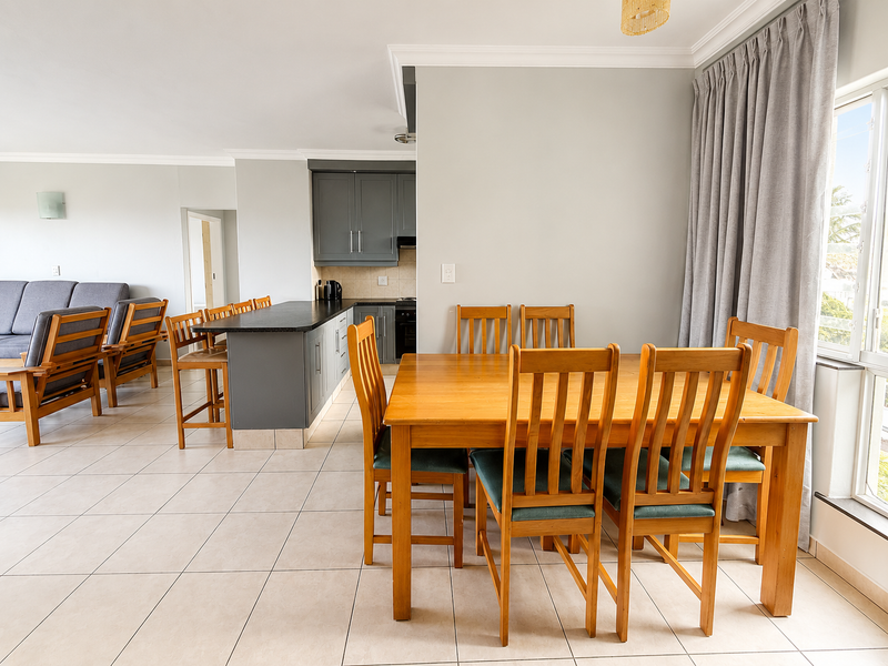 Spacious open-plan living and dining area featuring a modern kitchen with dark cabinetry, stone countertops, and neutral tiled flooring throughout.