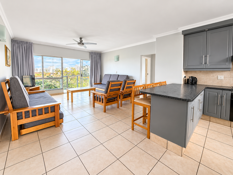 Open-plan living and kitchen area featuring grey cabinetry, dark countertops, ceramic tile flooring, and direct access to a balcony with scenic views.