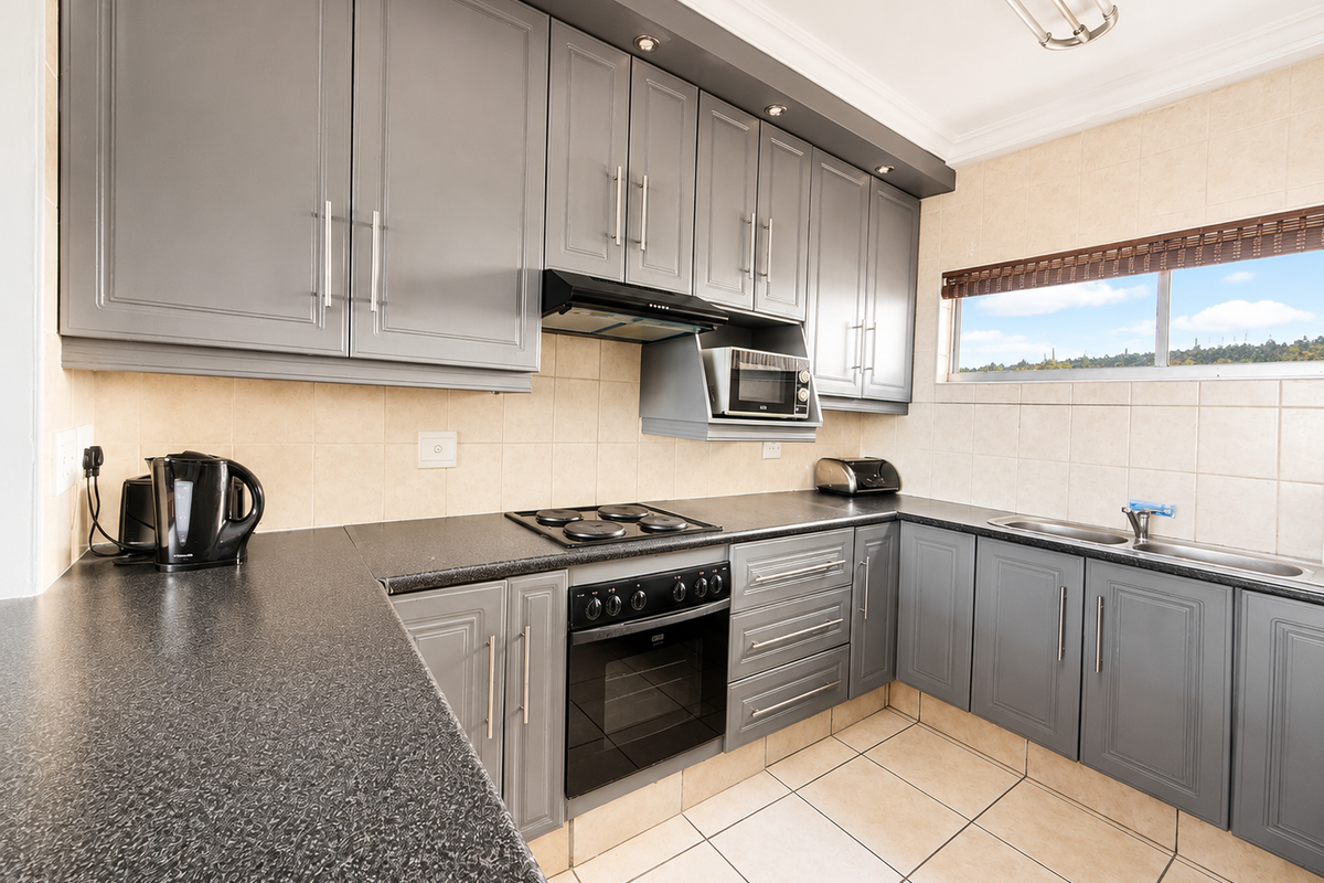 Modern kitchen featuring grey cabinetry, laminate countertops, built-in oven, electric hob, extractor fan, and a double sink with tiled backsplash.