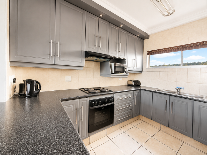 Modern kitchen featuring grey cabinetry, laminate countertops, built-in oven, electric hob, extractor fan, and a double sink with tiled backsplash.