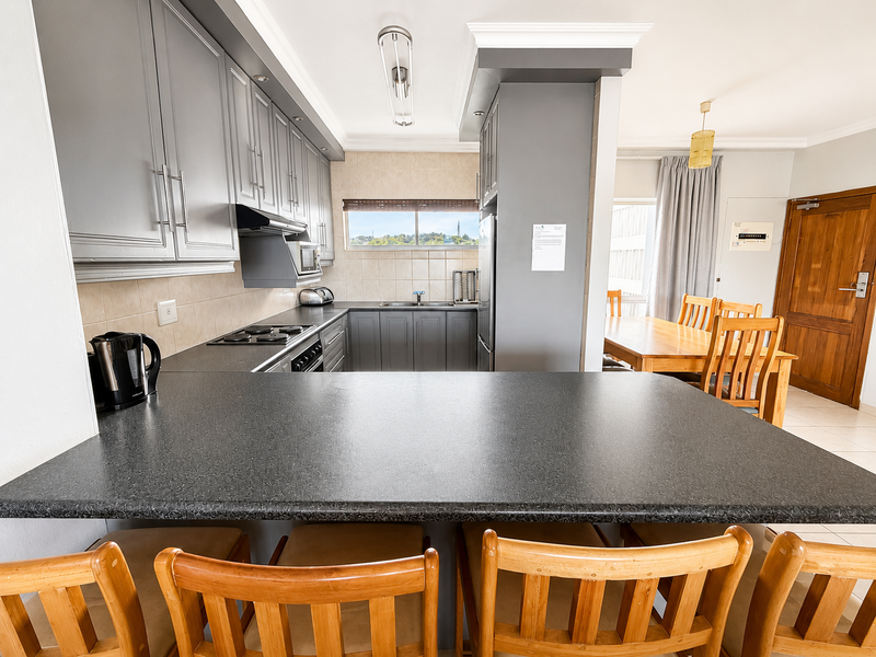 Open-plan kitchen featuring grey cabinetry, laminate countertops, built-in appliances, and a breakfast bar, seamlessly flowing into the adjacent dining area.