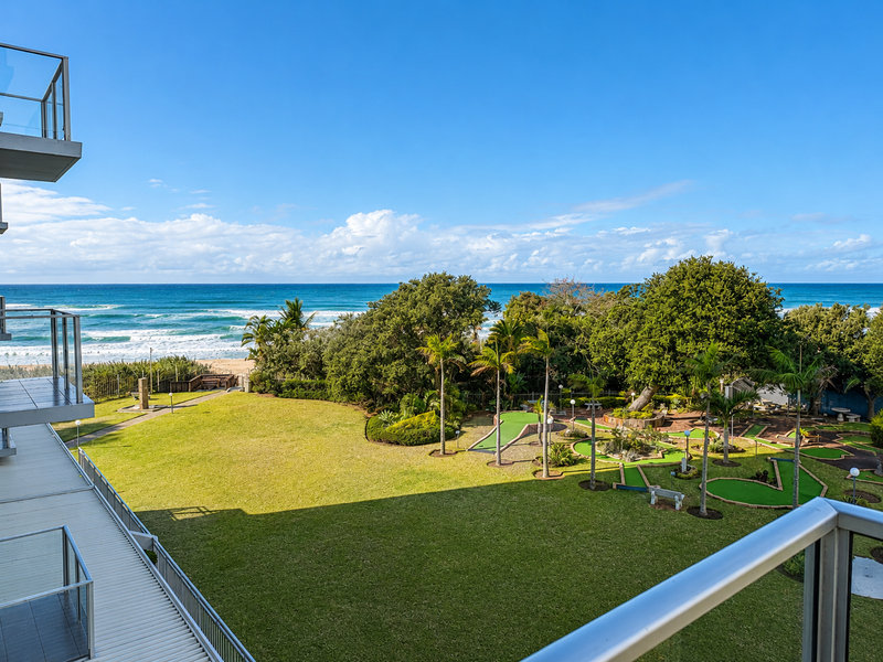 Elevated view from a balcony overlooking a landscaped garden, mini golf course, and the ocean coastline.