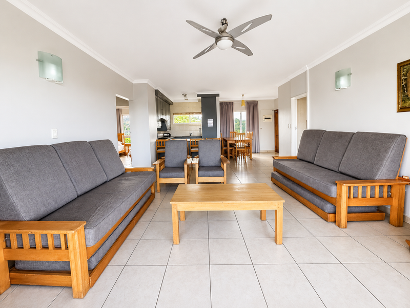 Spacious open-plan living and dining area featuring neutral tiled flooring, coved cornicing, and a central ceiling fan, flowing into a functional kitchen space.