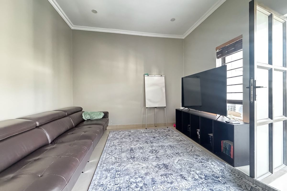 A well-maintained living room featuring neutral walls, recessed lighting, and a secure entrance door with security bars on the window.