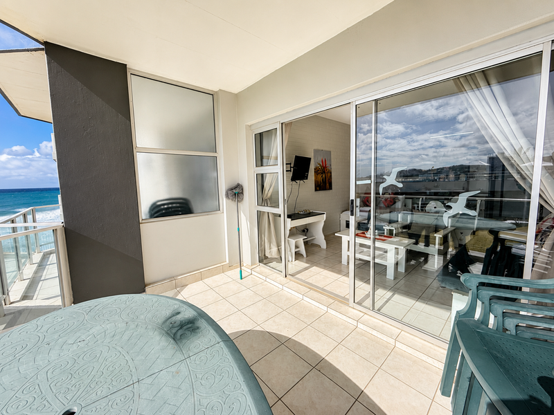 A covered balcony featuring tiled flooring, a metal balustrade, and sliding glass doors providing access to the interior living space with ocean views.