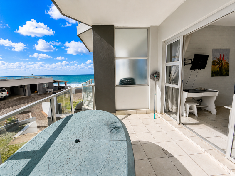 A spacious balcony featuring tiled flooring and a glass balustrade, offering direct access to the interior living area and scenic coastal views.