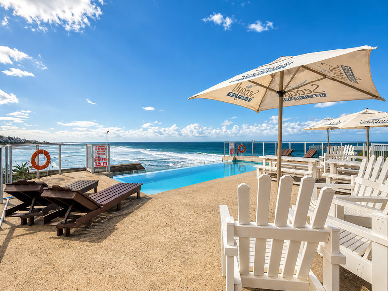 An elevated infinity pool area featuring a glass balustrade and expansive ocean views, providing a scenic outdoor relaxation space.