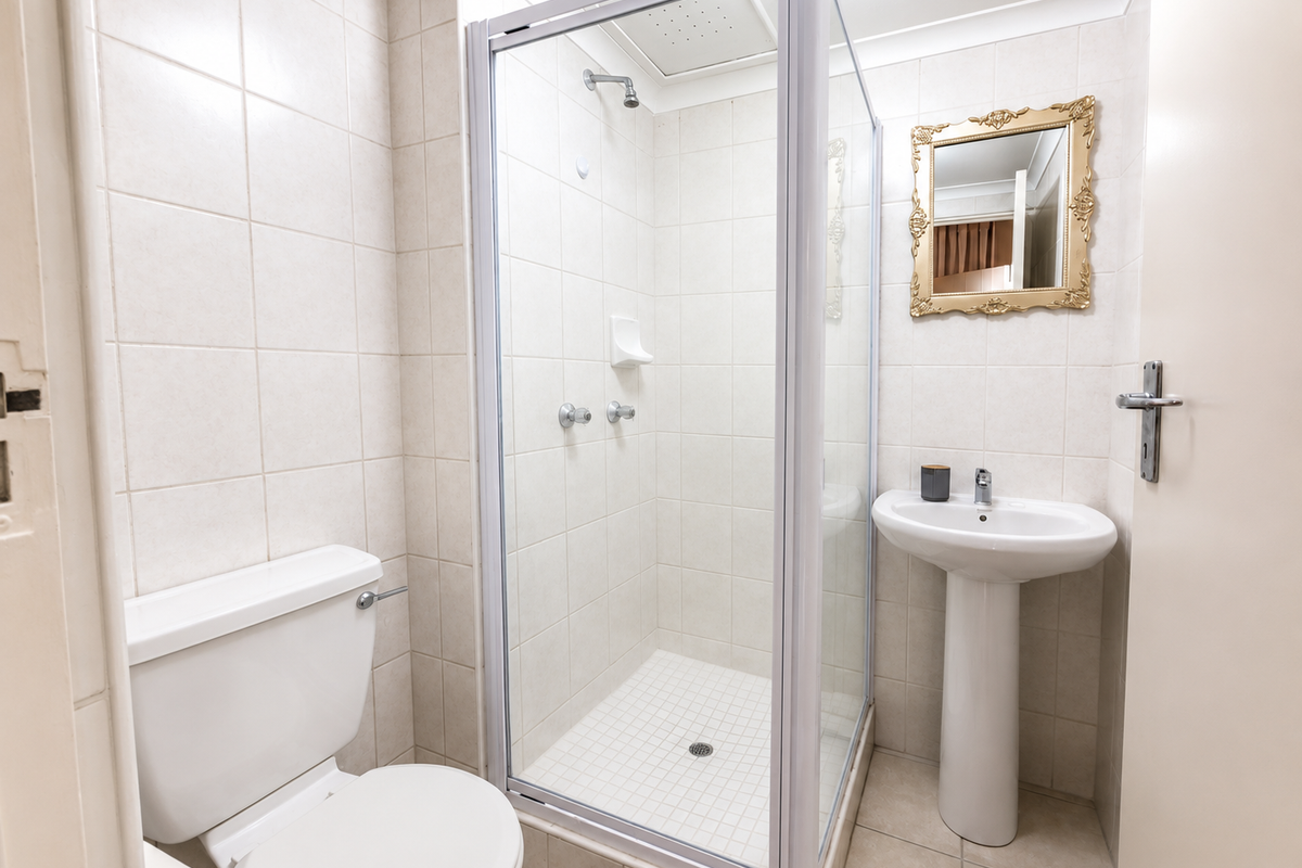 A clean, functional bathroom featuring a pedestal basin, a glass-enclosed shower, and neutral wall and floor tiling.