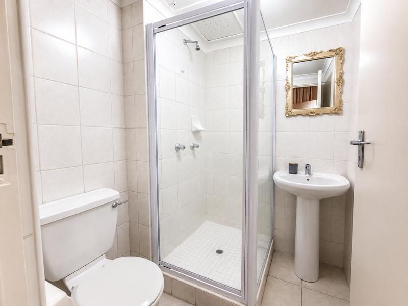 A clean, functional bathroom featuring a pedestal basin, a glass-enclosed shower, and neutral wall and floor tiling.