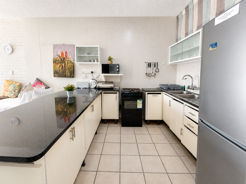 A functional kitchen featuring granite countertops, ample built-in cabinetry, a double basin sink, and a tiled backsplash with a freestanding stove.