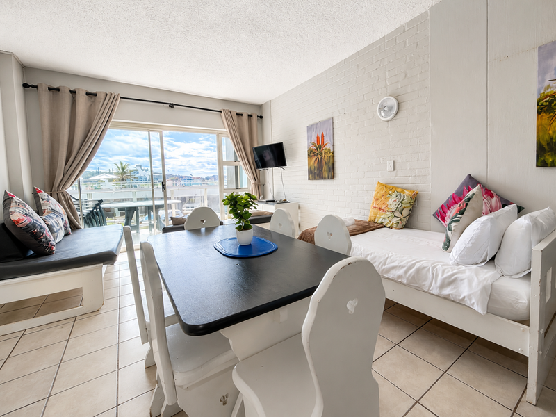 Open-plan living and dining area featuring ceramic floor tiles, a painted brick feature wall, and large sliding glass doors leading to a balcony.