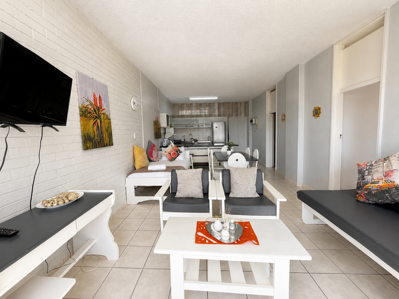 An open-plan living and kitchen area featuring tiled floors, a textured brick feature wall, and functional kitchen cabinetry.