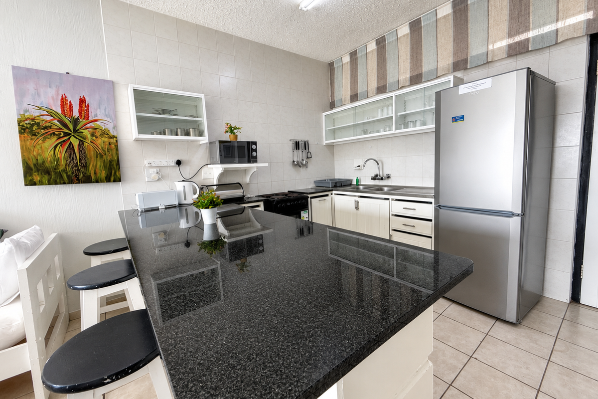 A functional kitchen featuring a large granite-topped breakfast island, ample built-in cabinetry, tiled backsplash, and integrated appliances in a well-maintained apartment setting.