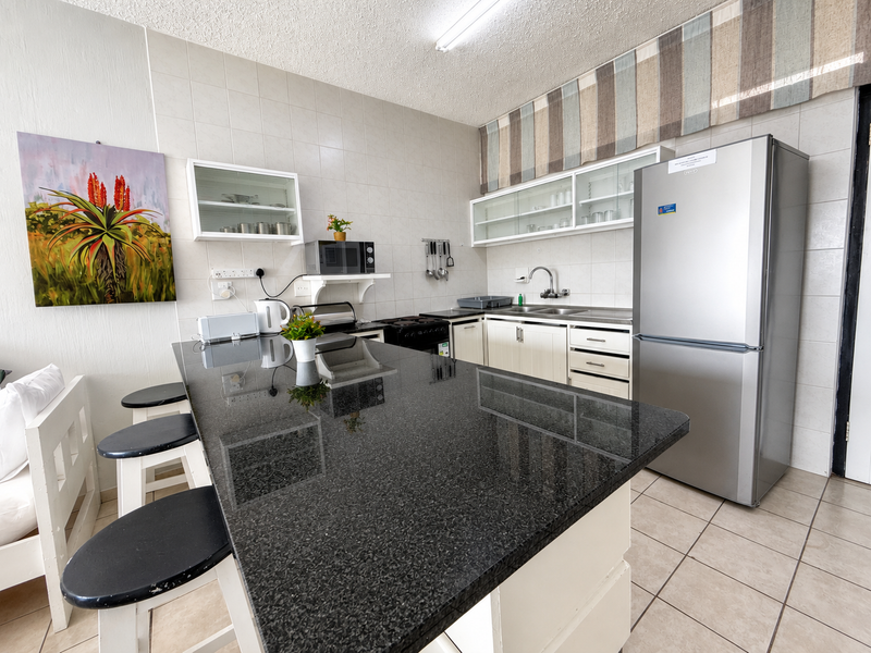 A functional kitchen featuring a large granite-topped breakfast island, ample built-in cabinetry, tiled backsplash, and integrated appliances in a well-maintained apartment setting.
