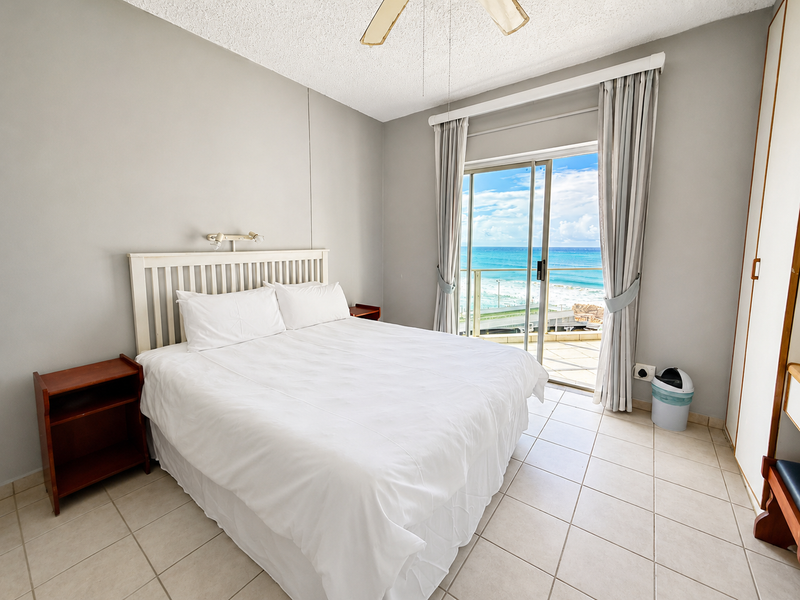 A bedroom featuring tiled flooring, a built-in wardrobe, and a sliding glass door that opens to a balcony with ocean views.