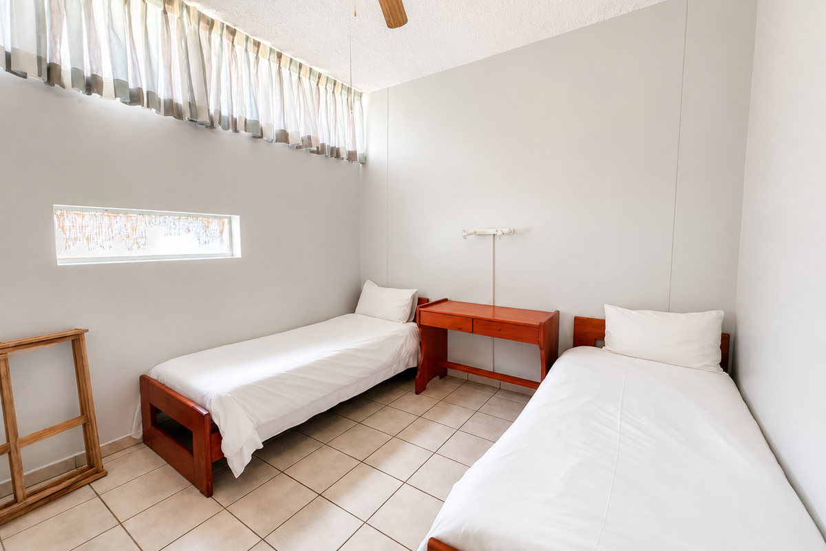 A functional bedroom featuring tiled flooring, a ceiling fan, and high-level windows providing natural light.