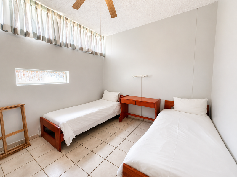 A functional bedroom featuring tiled flooring, a ceiling fan, and high-level windows providing natural light.