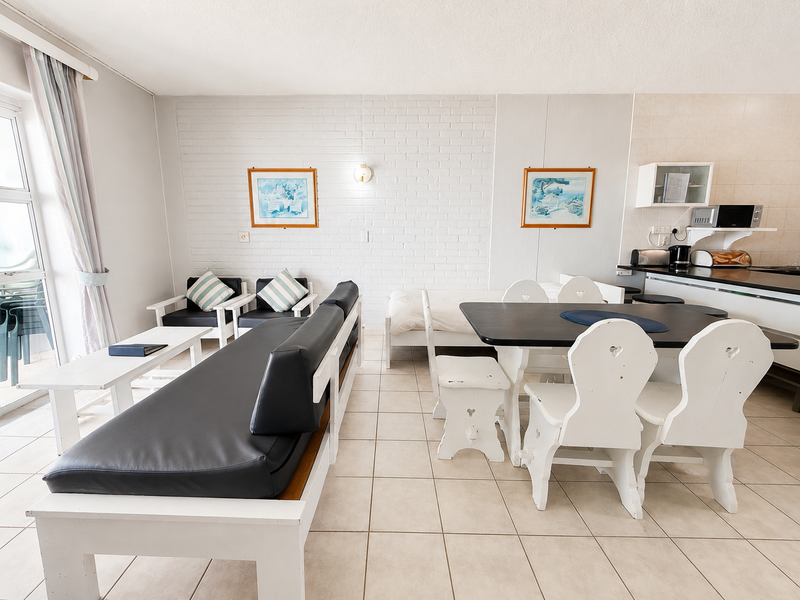 Open plan living and dining area featuring tiled floors, a painted brick feature wall, and direct access to an outdoor balcony.