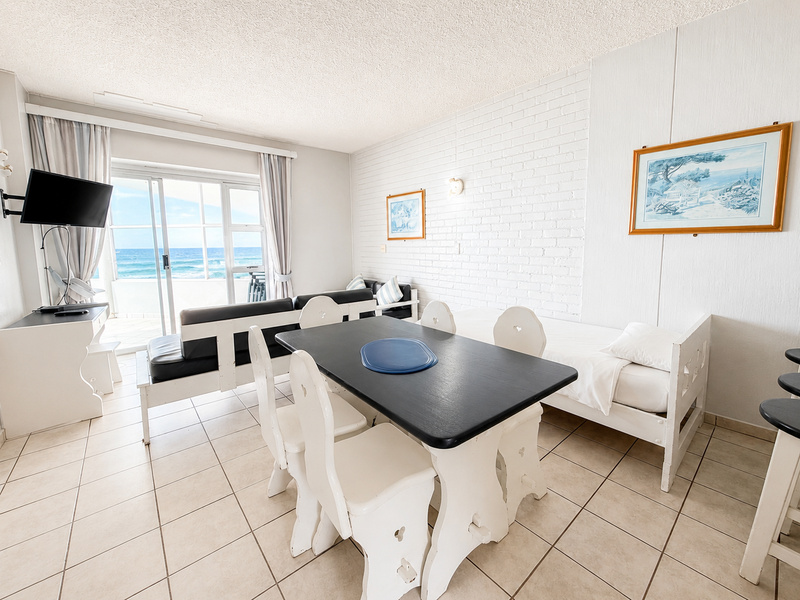 Open-plan living and dining area featuring ceramic floor tiles, a painted brick feature wall, and direct access to a balcony with ocean views.